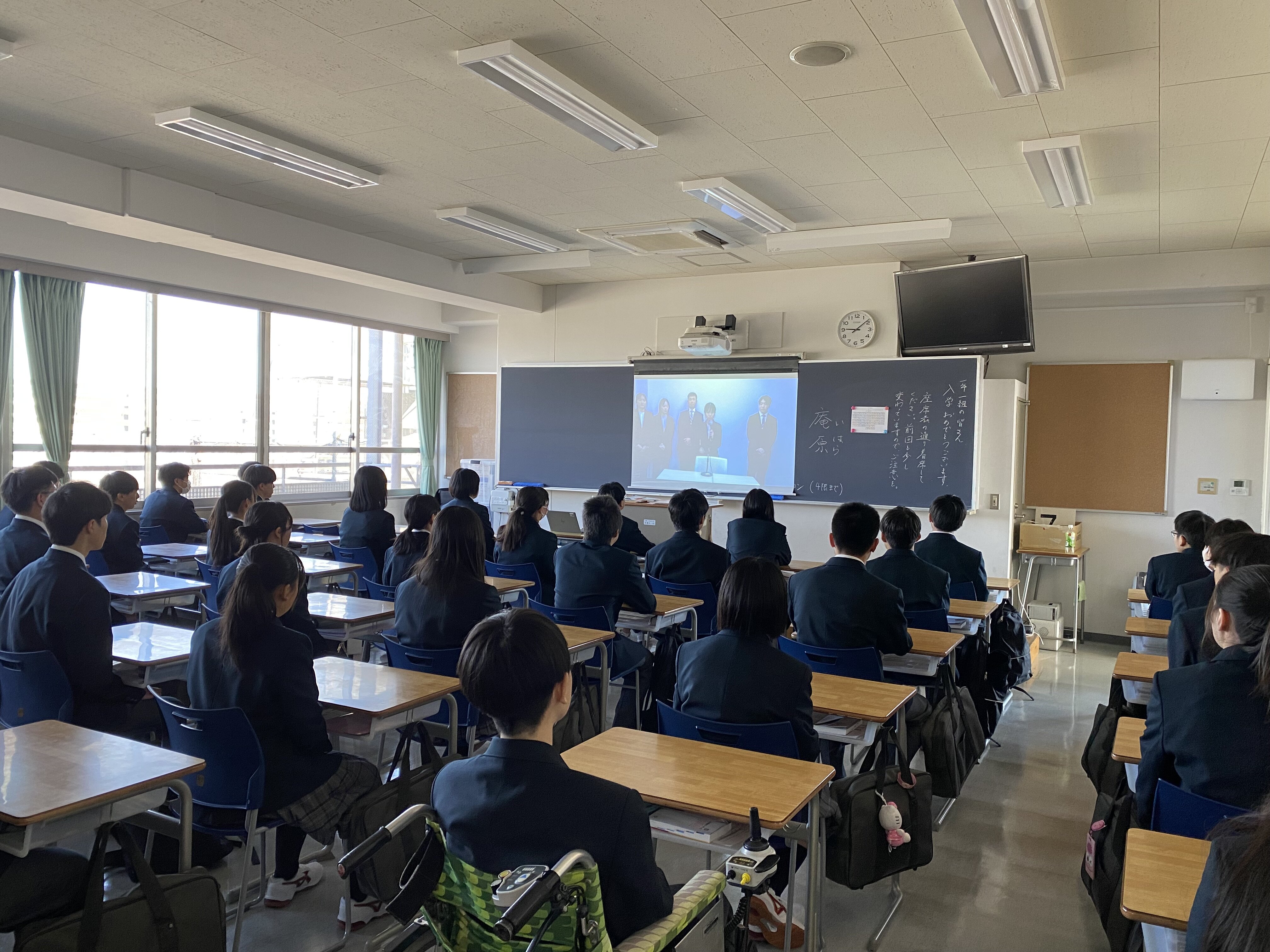 新任の先生の紹介を校内放送で見守る1年1組の様子